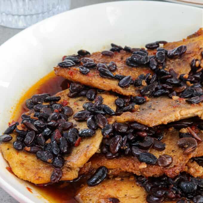 Tilapia fillets in a spicy tausi and garlic sauce on a white serving platter.