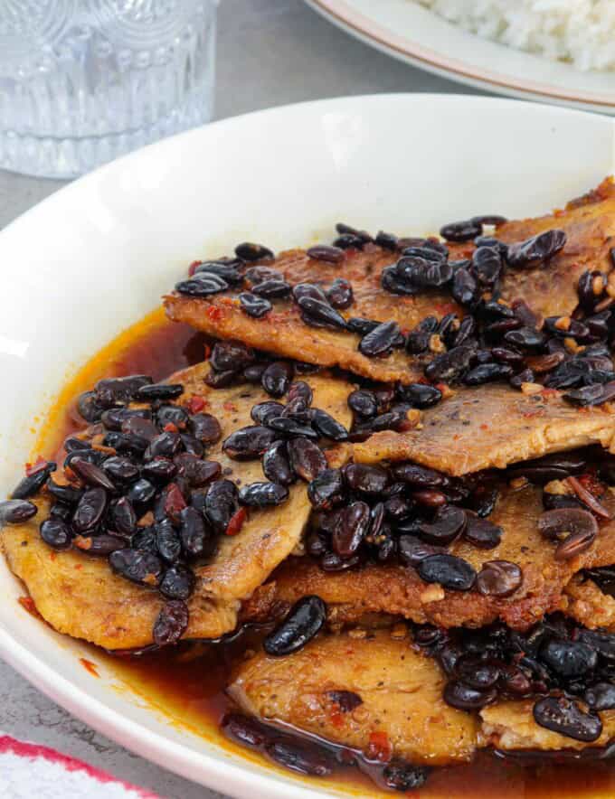 Tilapia fillets in a spicy tausi and garlic sauce on a white serving platter.