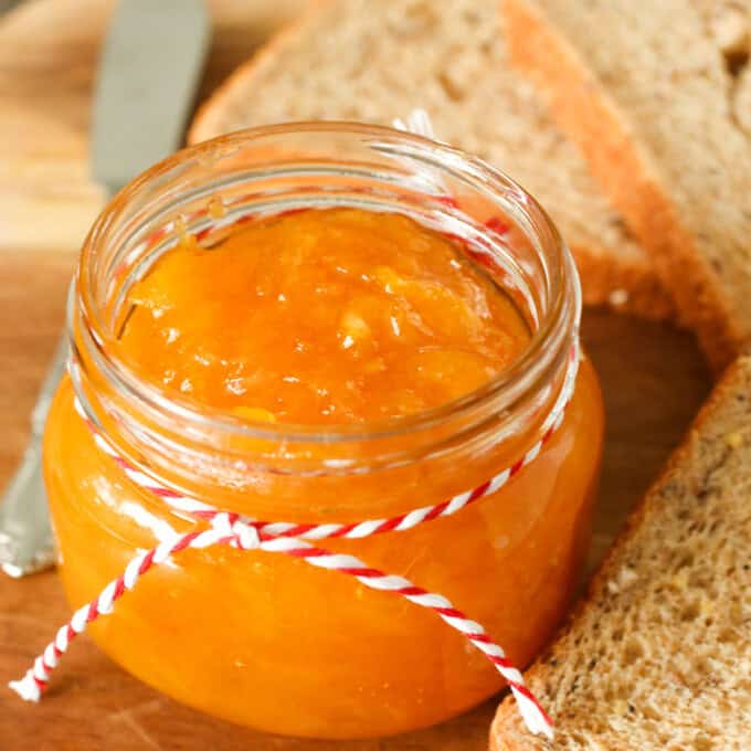 Mango Jam in a mason jar with wheat bread slices in the background.