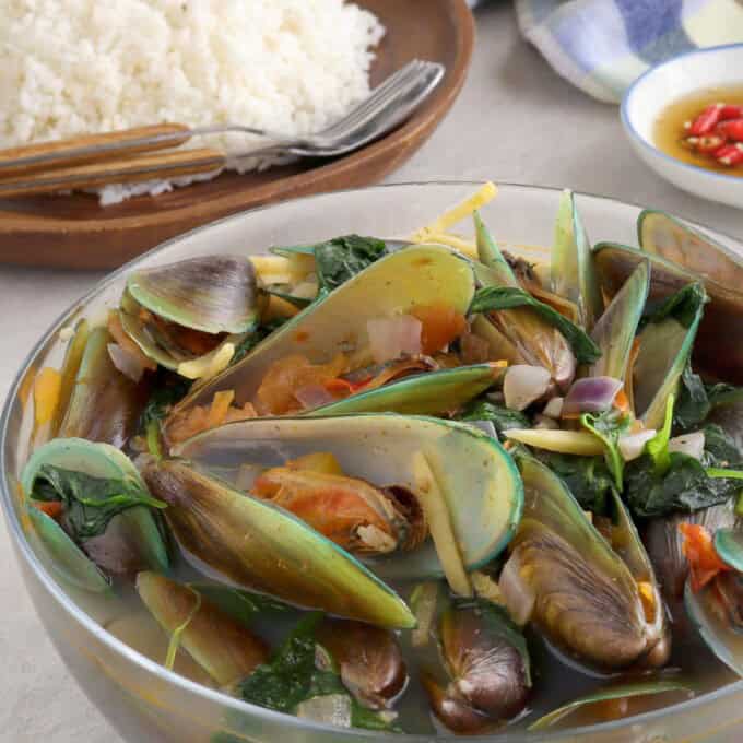 mussel soup in a bowl with a plate of steamed rice in the background.