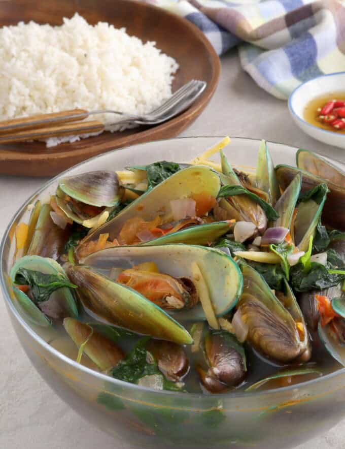 mussel soup in a bowl with a plate of steamed rice in the background.