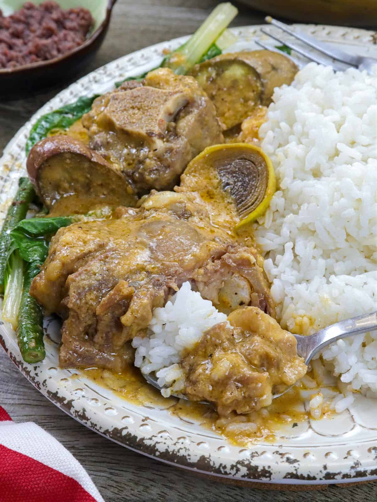 eating kare-kareng oxtail on a serving plate with steamed rice on the side.