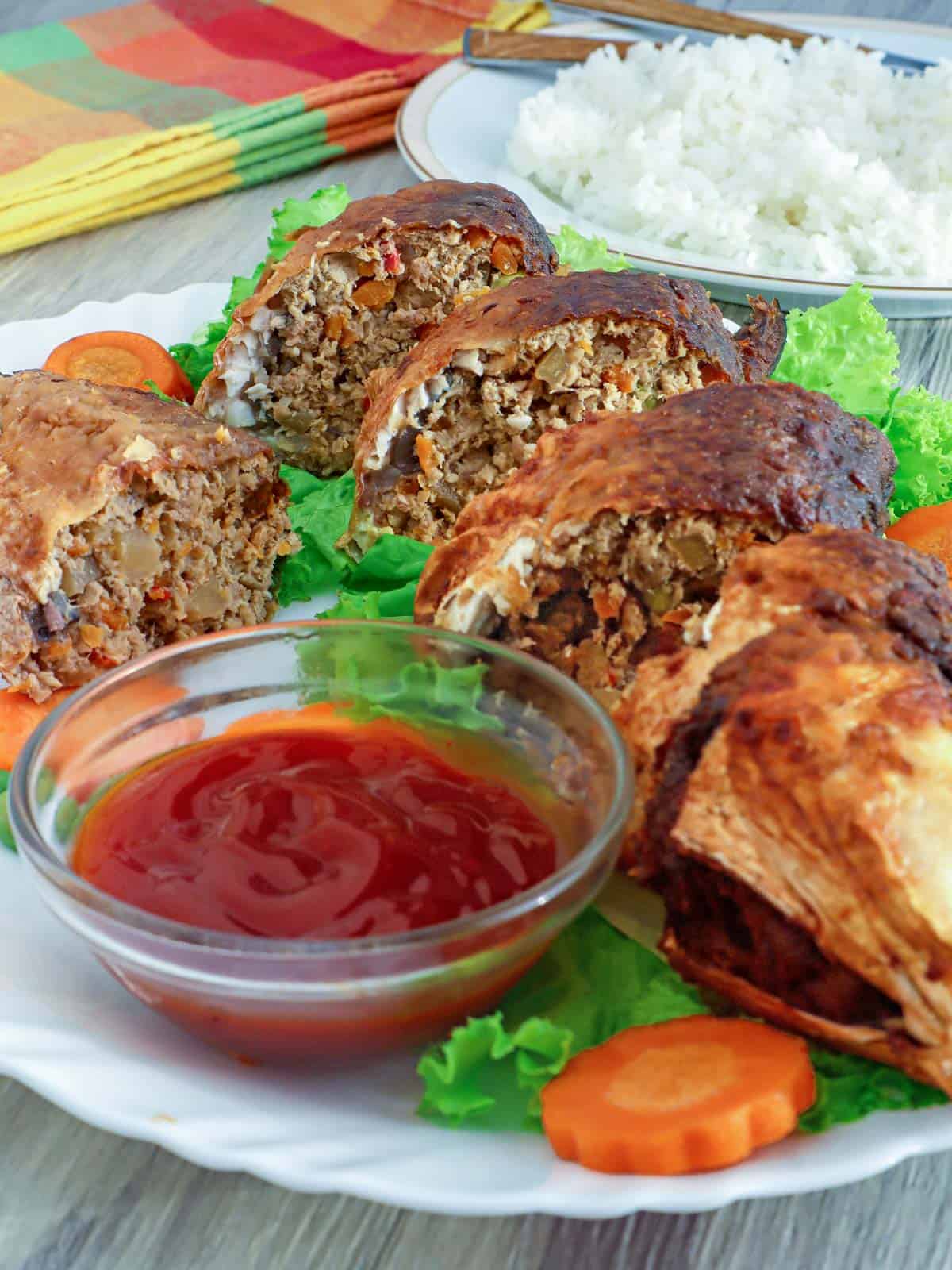 sliced stuffed milkfish on a platter with a small bowl of catsup on the side.