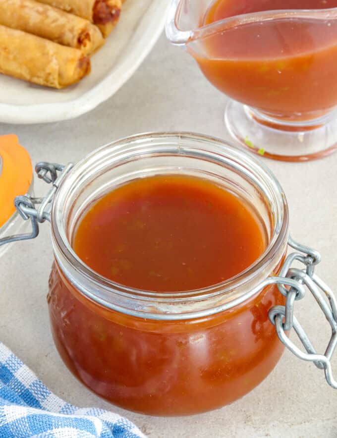 Sweet and Sour Sauce in a glass jar wtih fried lumpia in the background.