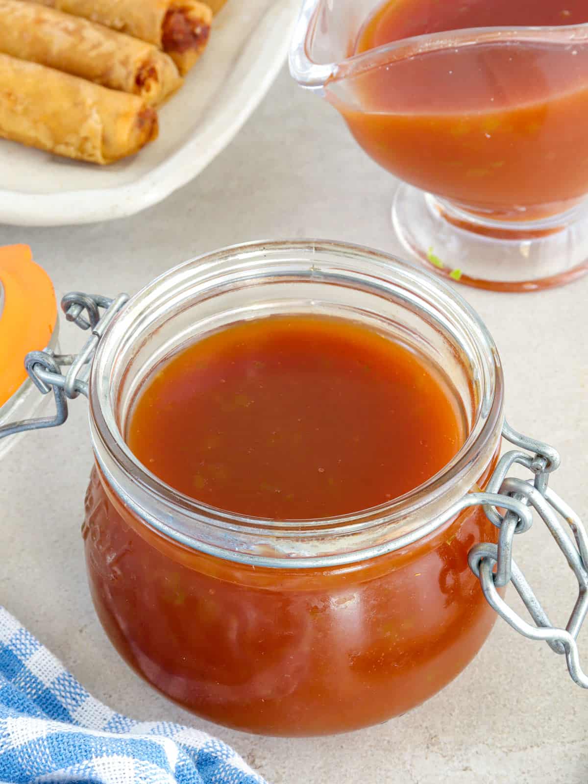 Sweet and Sour Sauce in a glass jar wtih fried lumpia in the background.