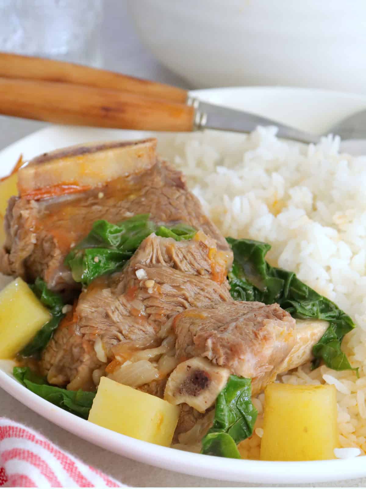 beef and pechay soup with steamed rice on a white plate.