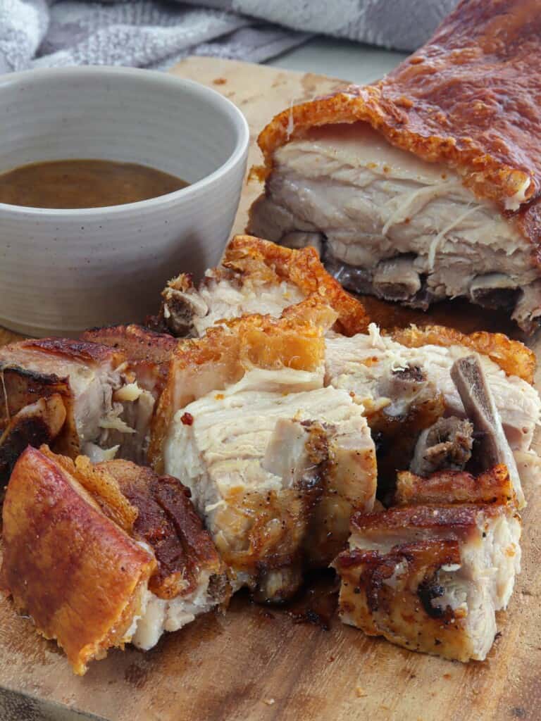 chopped Lechon sa Hurno on a wooden cutting board with a bowl of dipping sauce on the side.