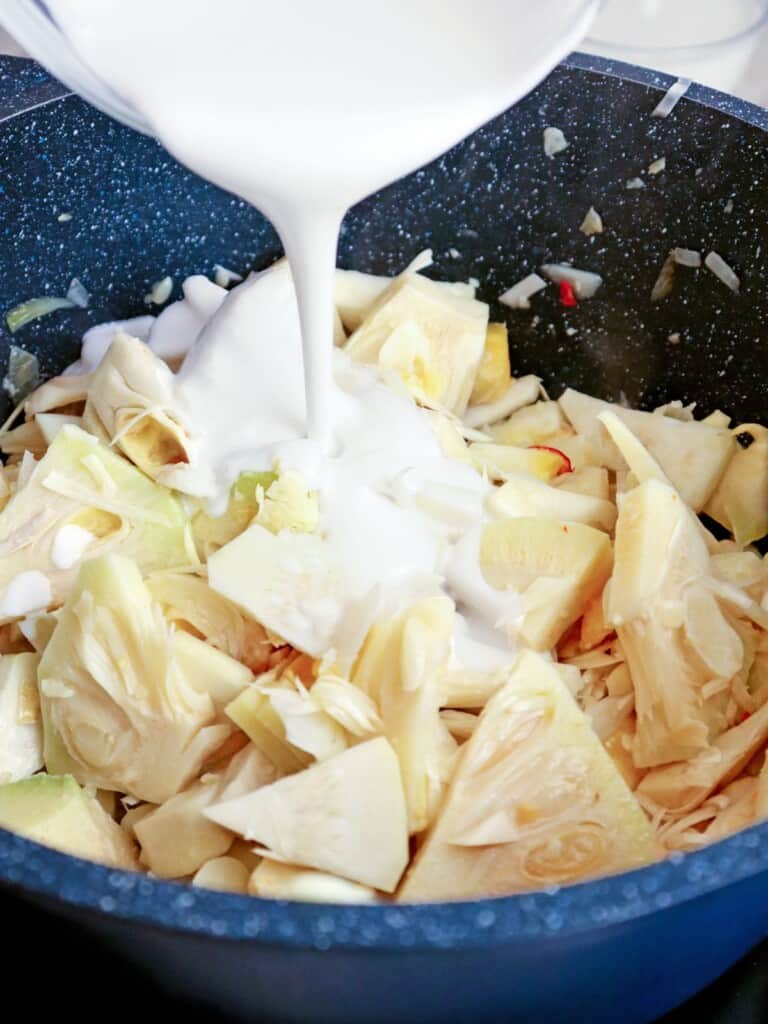 adding coconut milk to a pan of sliced jackfruit