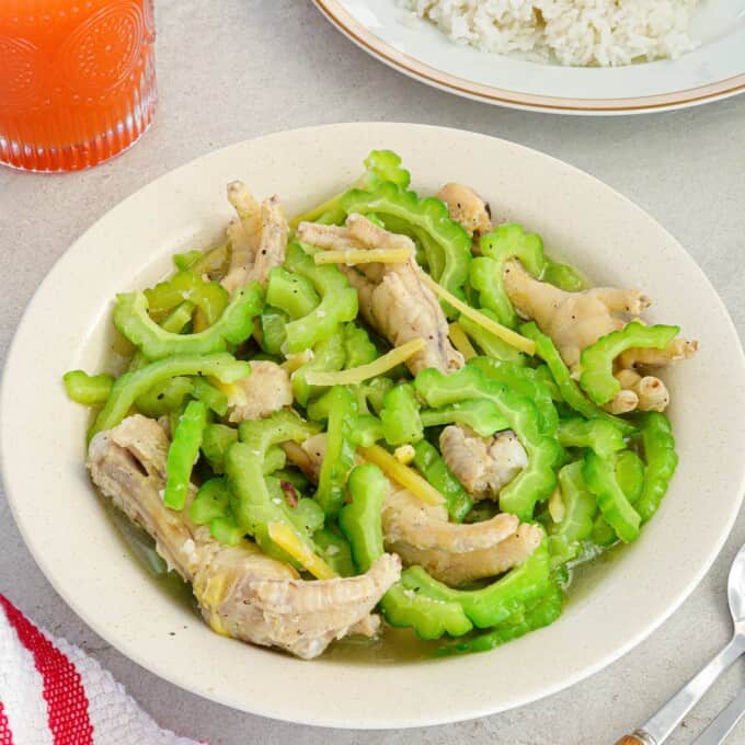 Ampalaya with Chicken Feet in a white bowl with a plate of steamed rice in the background.