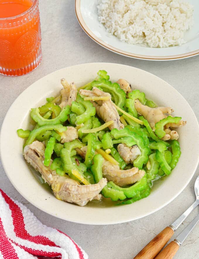 Ampalaya with Chicken Feet in a white bowl with a plate of steamed rice in the background.