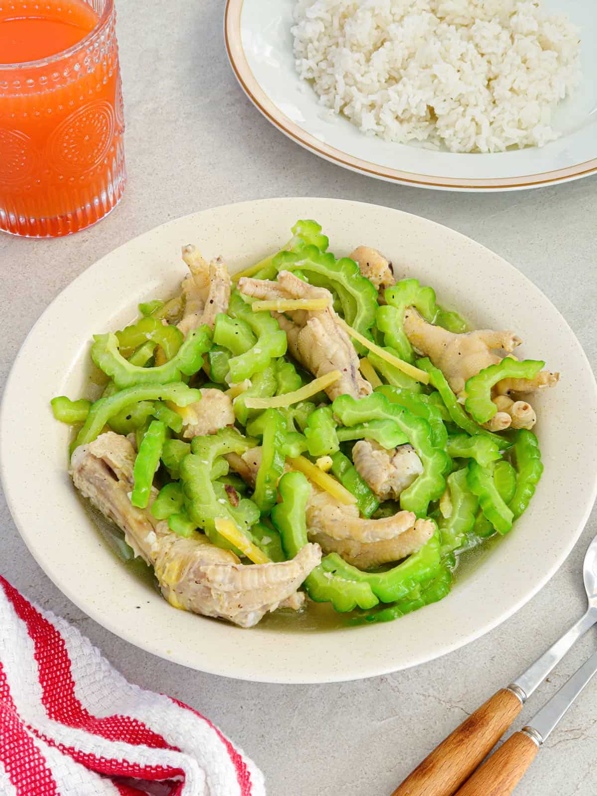 Ampalaya with Chicken Feet in a white bowl with a plate of steamed rice in the background.