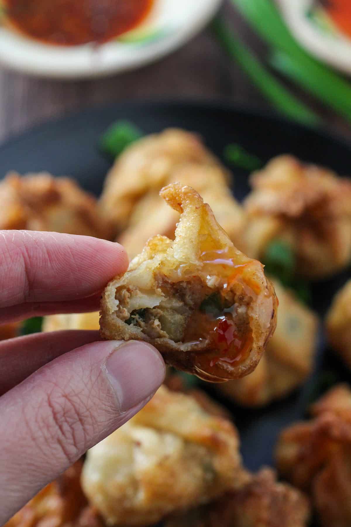 holding bitten longganisa wontons dipped in sweet chili sauce with fingers.