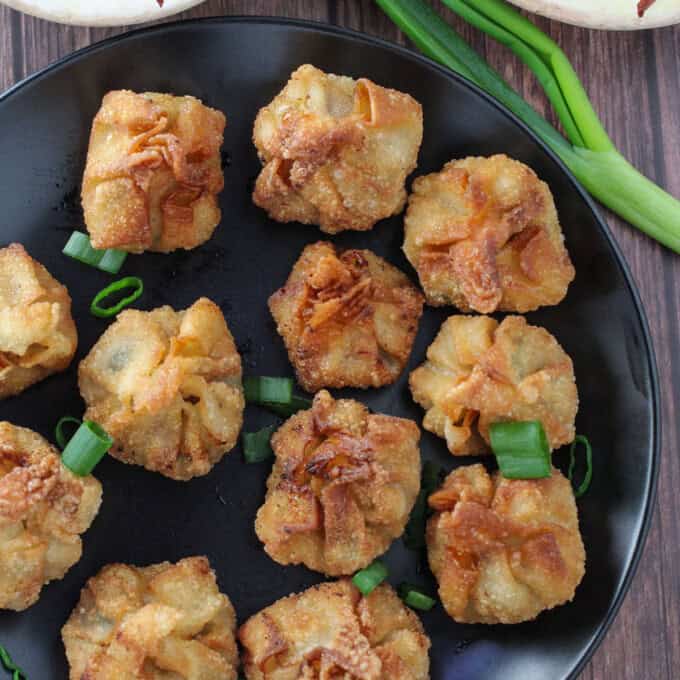 crispy fried longganisa wontons on a black plate with bowls of sweet chili sauce in the background.