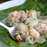 eating pinais na hipon with a spoon on a banana leaf-lined white plate.