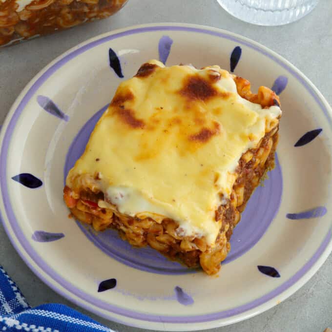 slice of baked macaroni with cheese topping on a white serving plate.