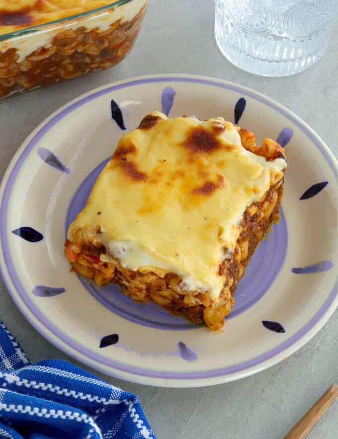 slice of baked macaroni with cheese topping on a white serving plate.