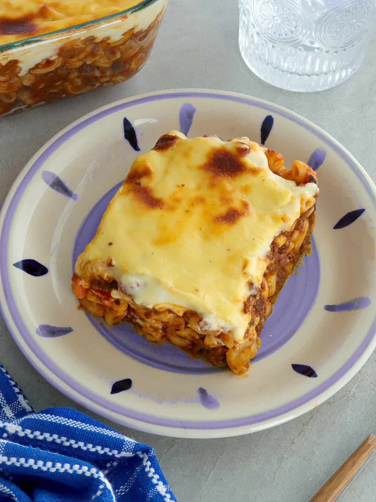 slice of baked macaroni with cheese topping on a white serving plate.