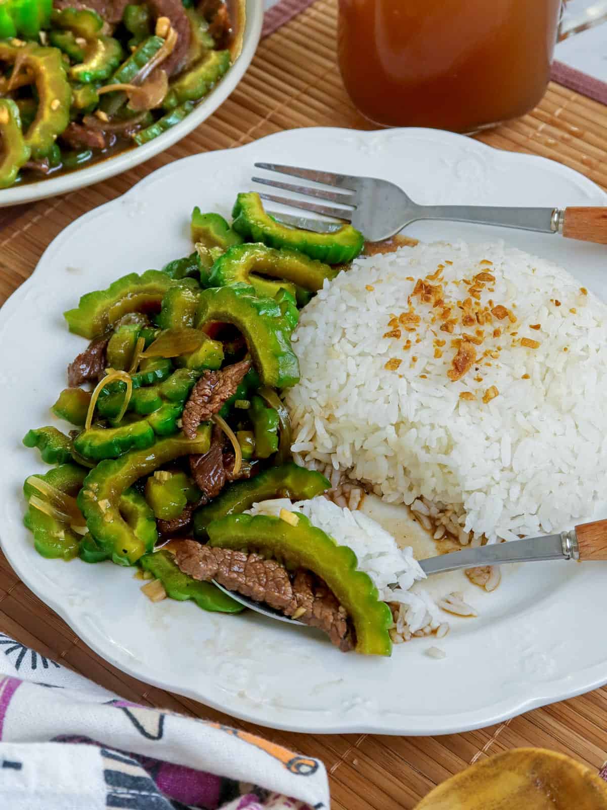 bittermelon and beef stir fry with steamed rice on a white plate.
