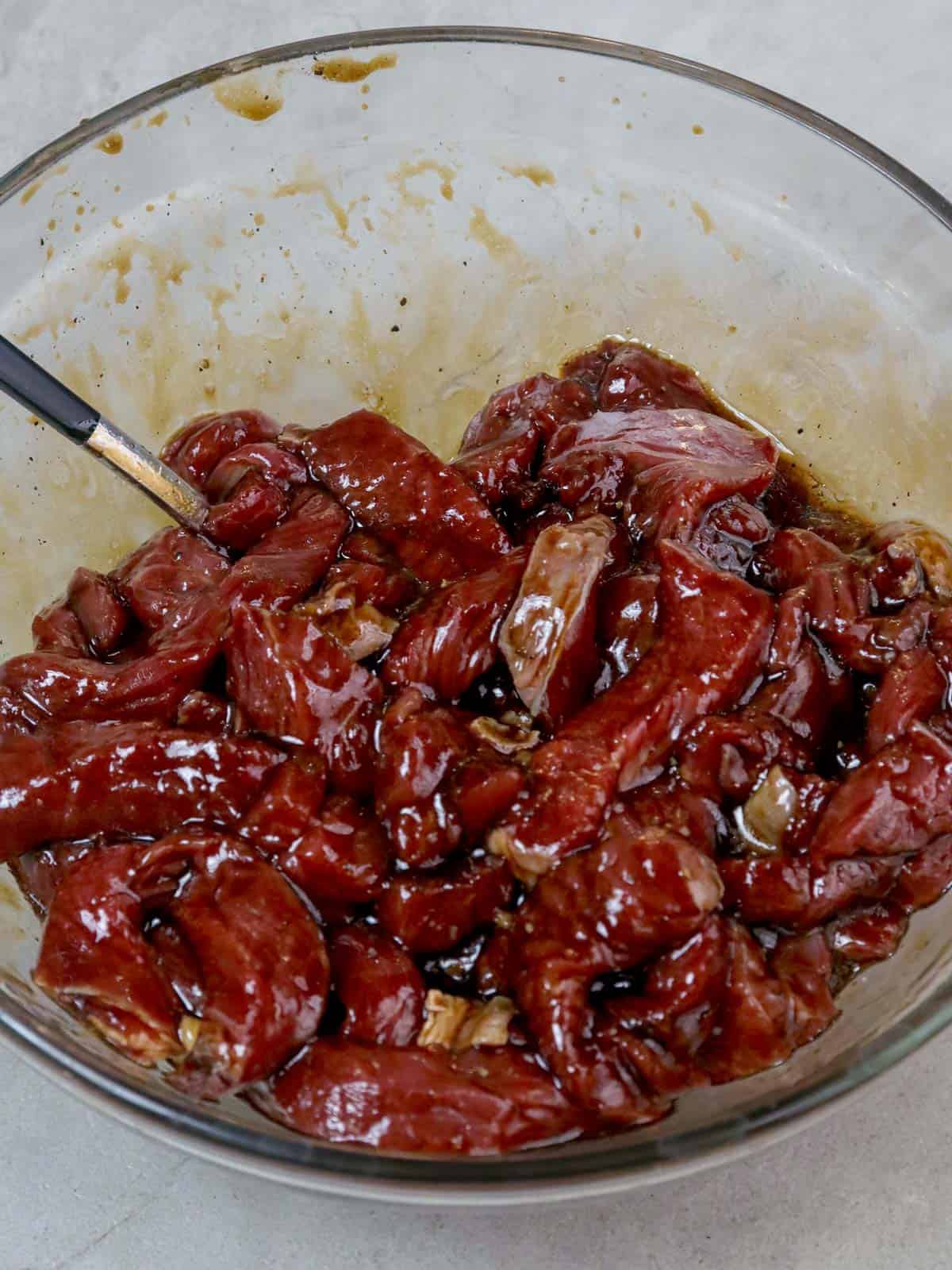 marinating beef strips in soy sauce, oyster sauce, and cornstarch in a glass bowl.