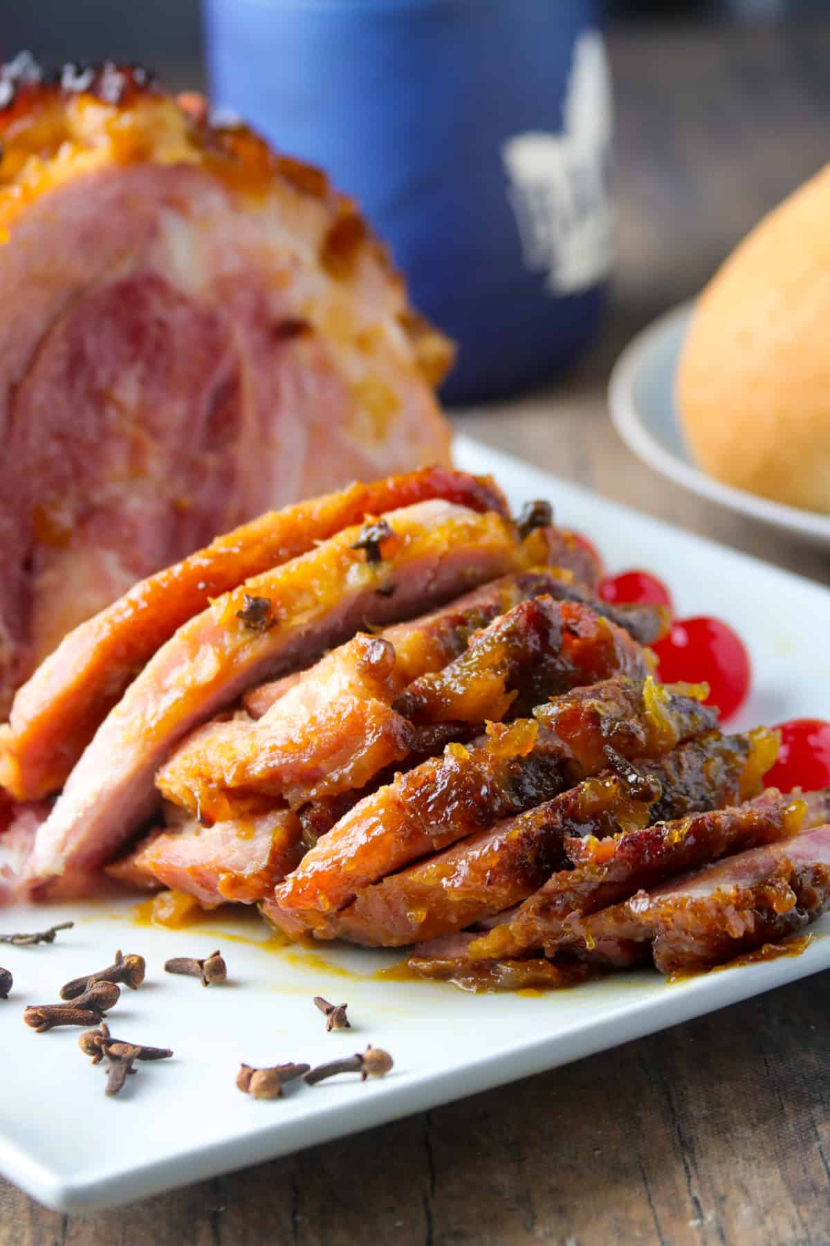 sliced Filipino-style Pineapple Glazed Ham on a white platter with dinner rolls in the background.