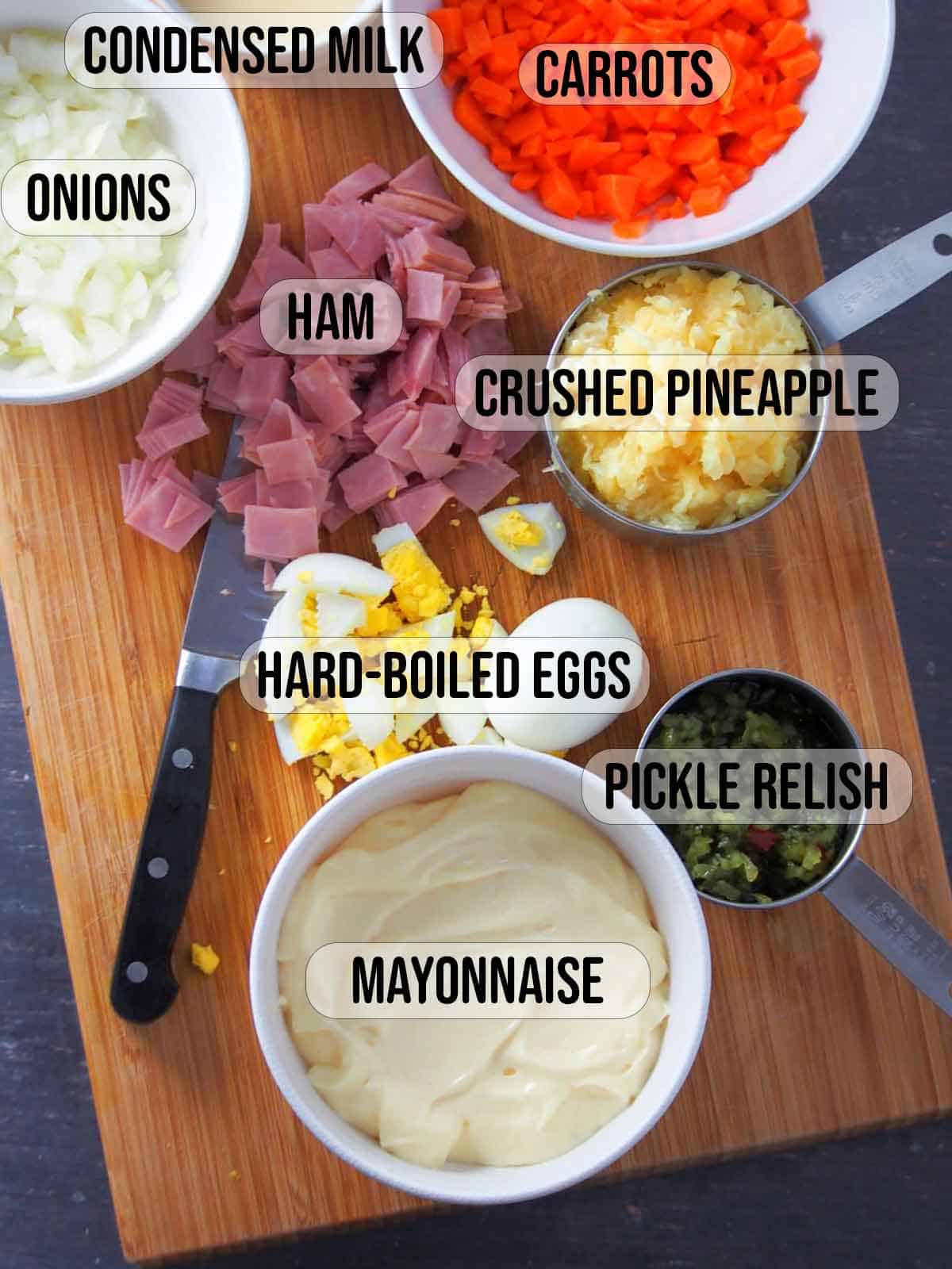 chopped ham, boiled eggs, diced carrots, crushed pineapple, chopped onions, mayonnaise, sweet relish on a wooden board.