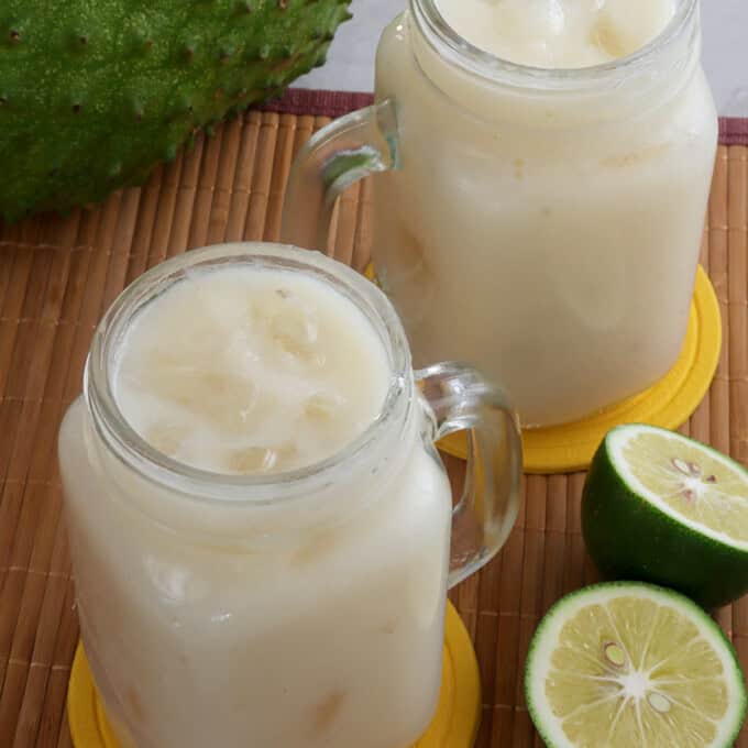 soursop juice in mason glasses with lime halves and soursop fruit in the background.