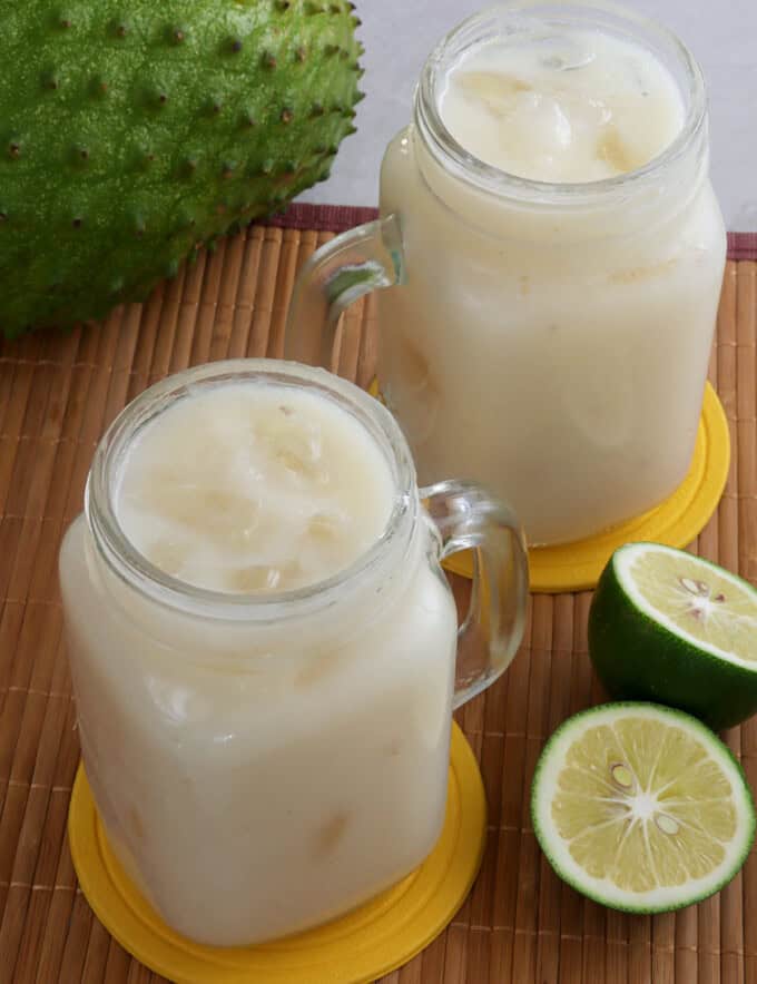 soursop juice in mason glasses with lime halves and soursop fruit in the background.