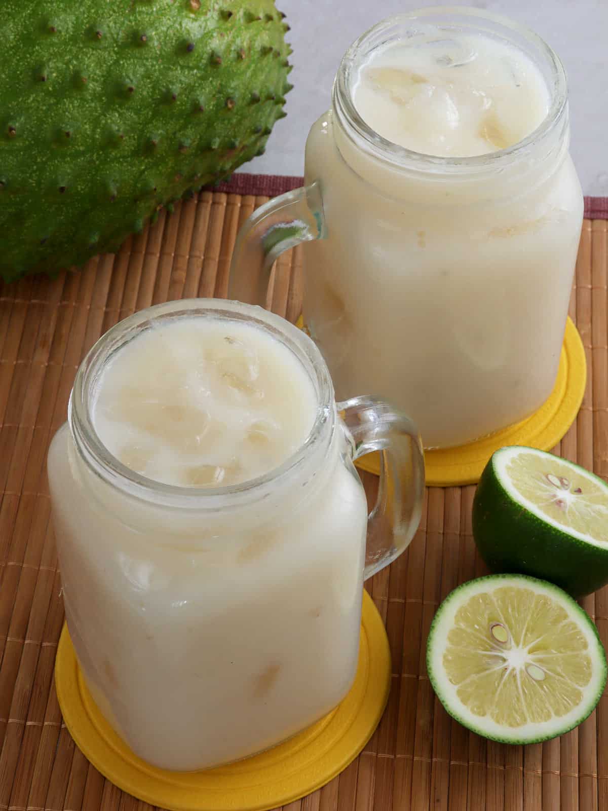 soursop juice in mason glasses with lime halves and soursop fruit in the background.