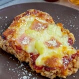 crispy breaded chicken breast baked with cheese, ham, and pineapple toppings on a brown plate.