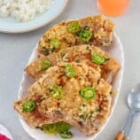 salt and pepper pork chops on a white platter with a plate of steamed rice in the background.