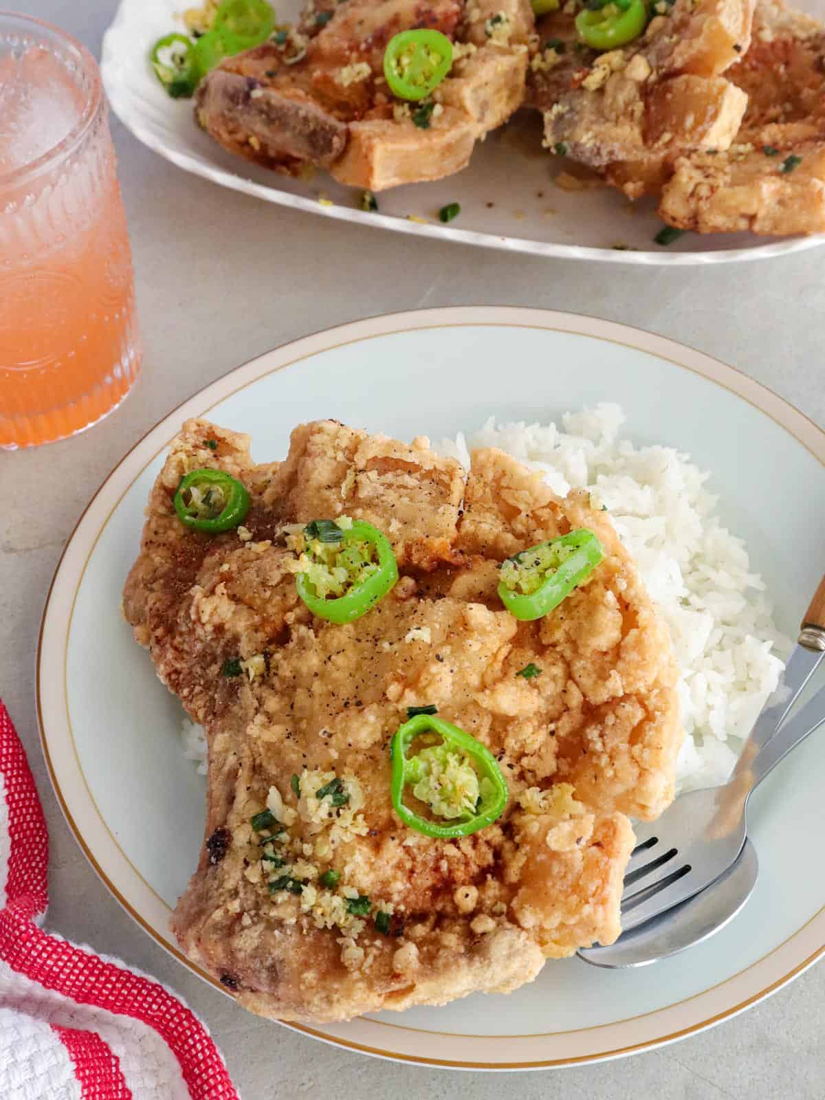 salt and pepper pork chops on a white plate with a side of steamed rice.