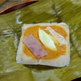 filipino tamales topped with flaked chicken and and hard boiled eggs on a serving plate.