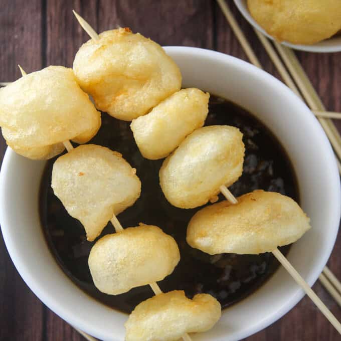 fried fish balls skewered in bamboo sticks on top of a bowl of fish ball sauce.