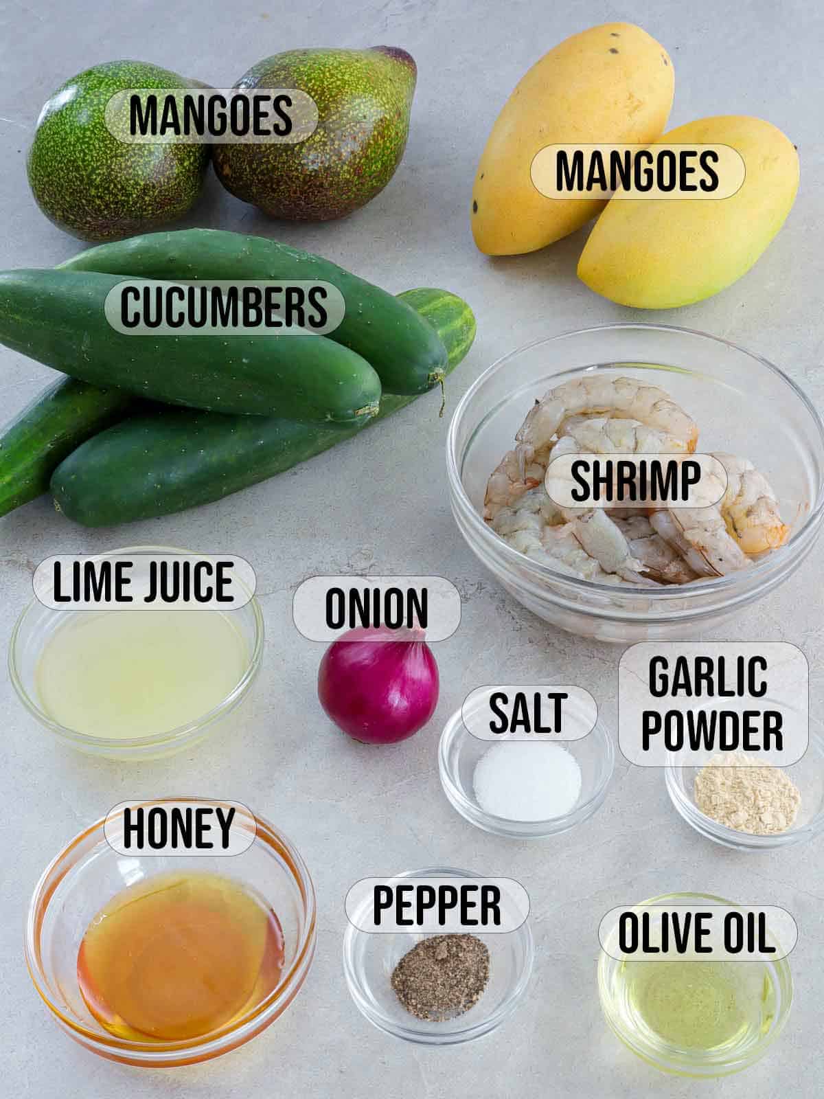 cucumbers, mangoes, avocadoes, shrimp, honey, onions, lime juice, salt, pepper, garlic powder, pepper in bowls.