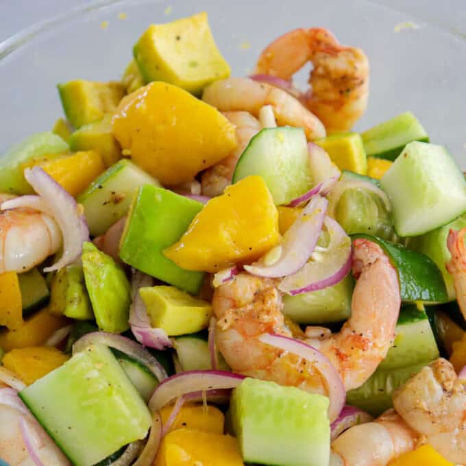 mango avocado cucumber salad with grilled shrimp on a white serving plate