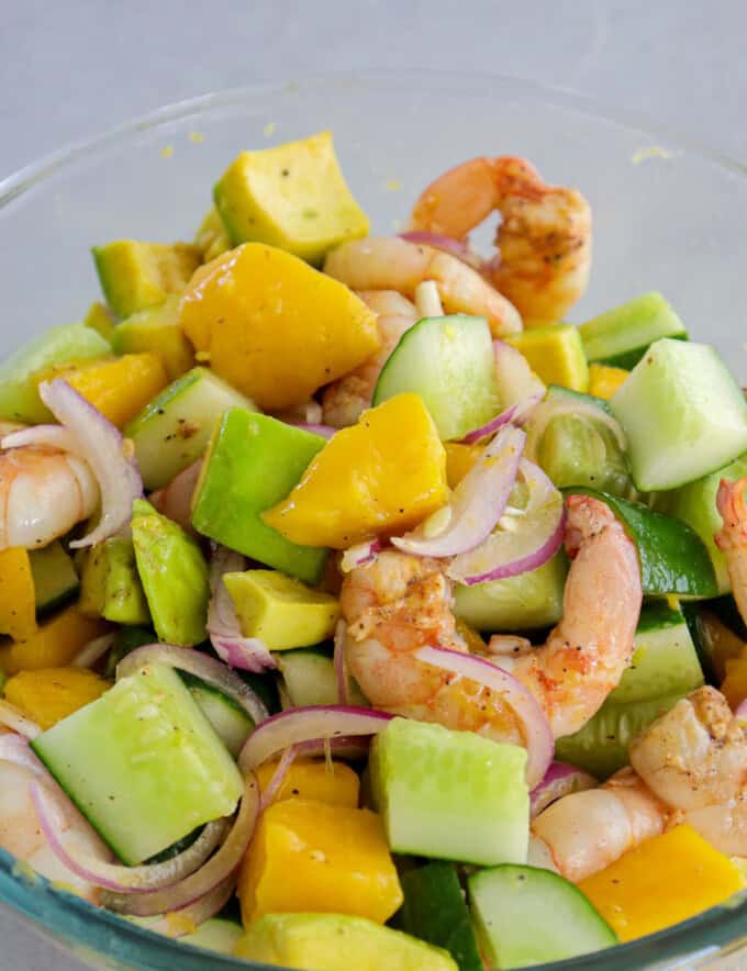 mango avocado cucumber salad with grilled shrimp on a white serving plate