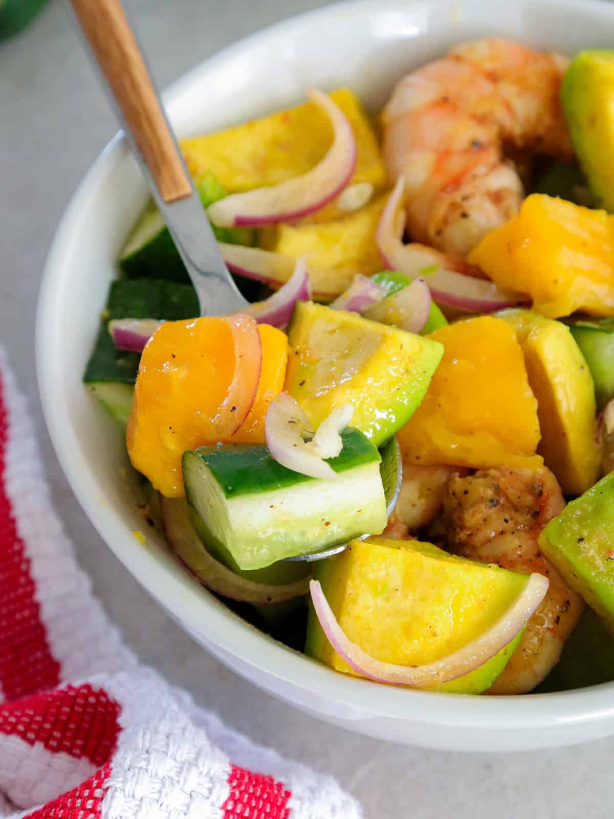 mango avocado cucumber salad with grilled shrimp on a white serving bowl.