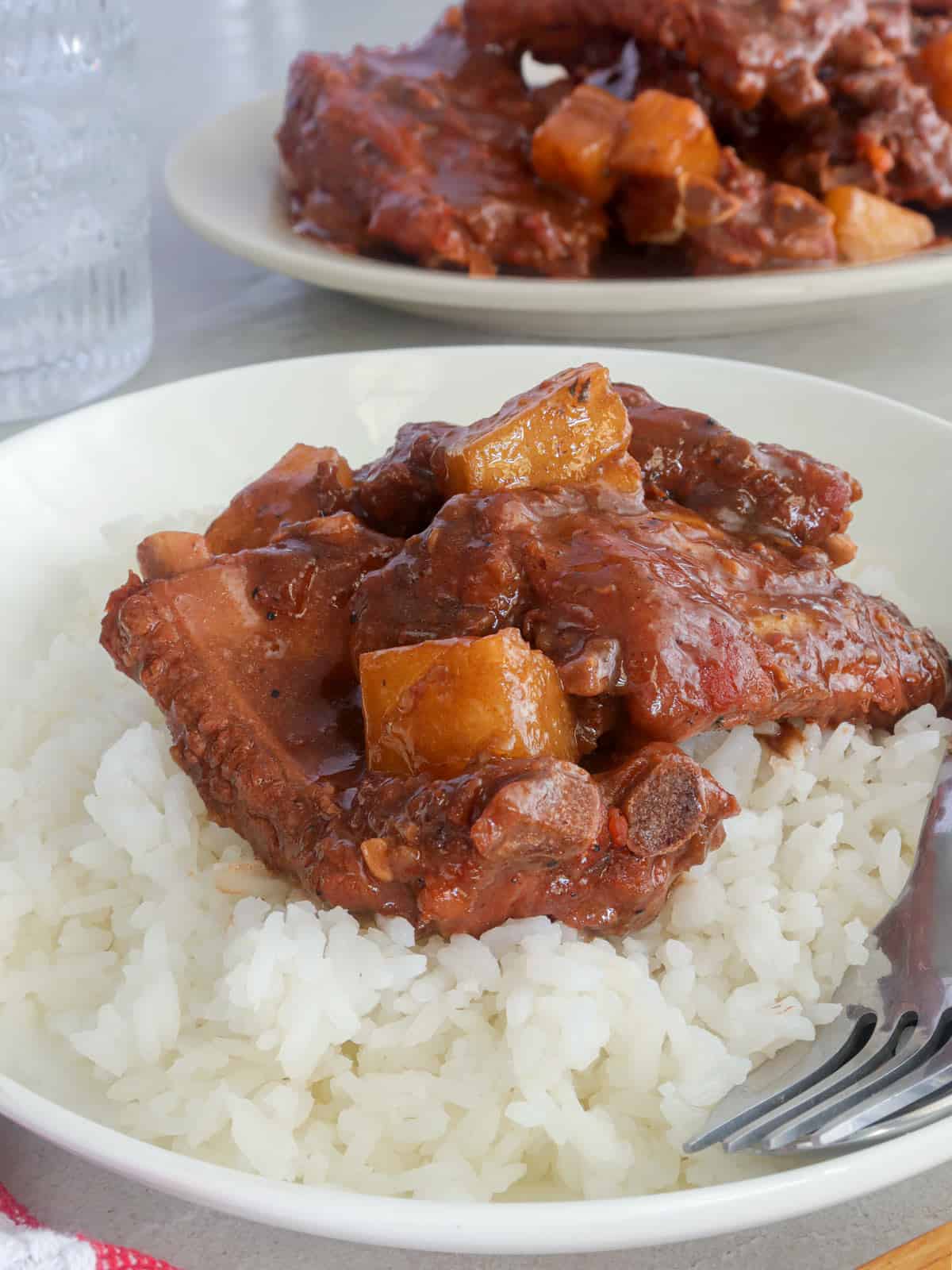braised Spare Ribs with Ketchup and Pineapples on a bed of steamed rice on a white plate.
