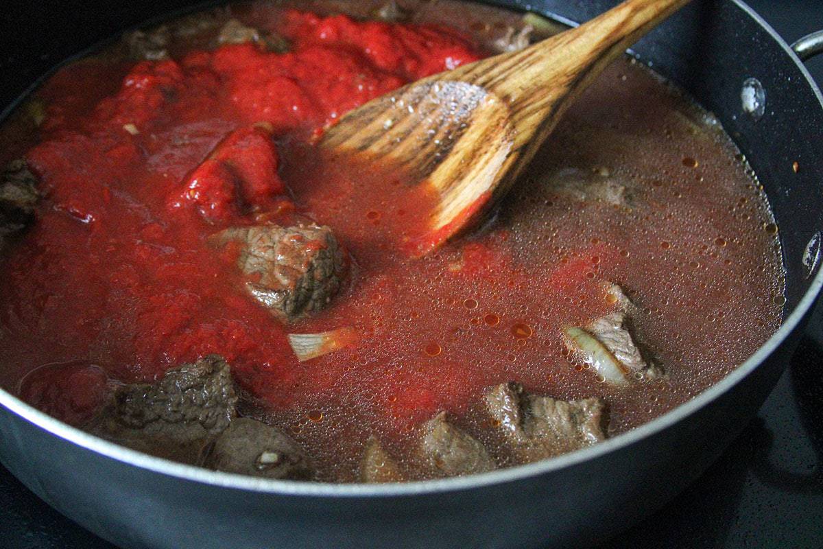 stirring tomato sauce with the beef and broth in a pan