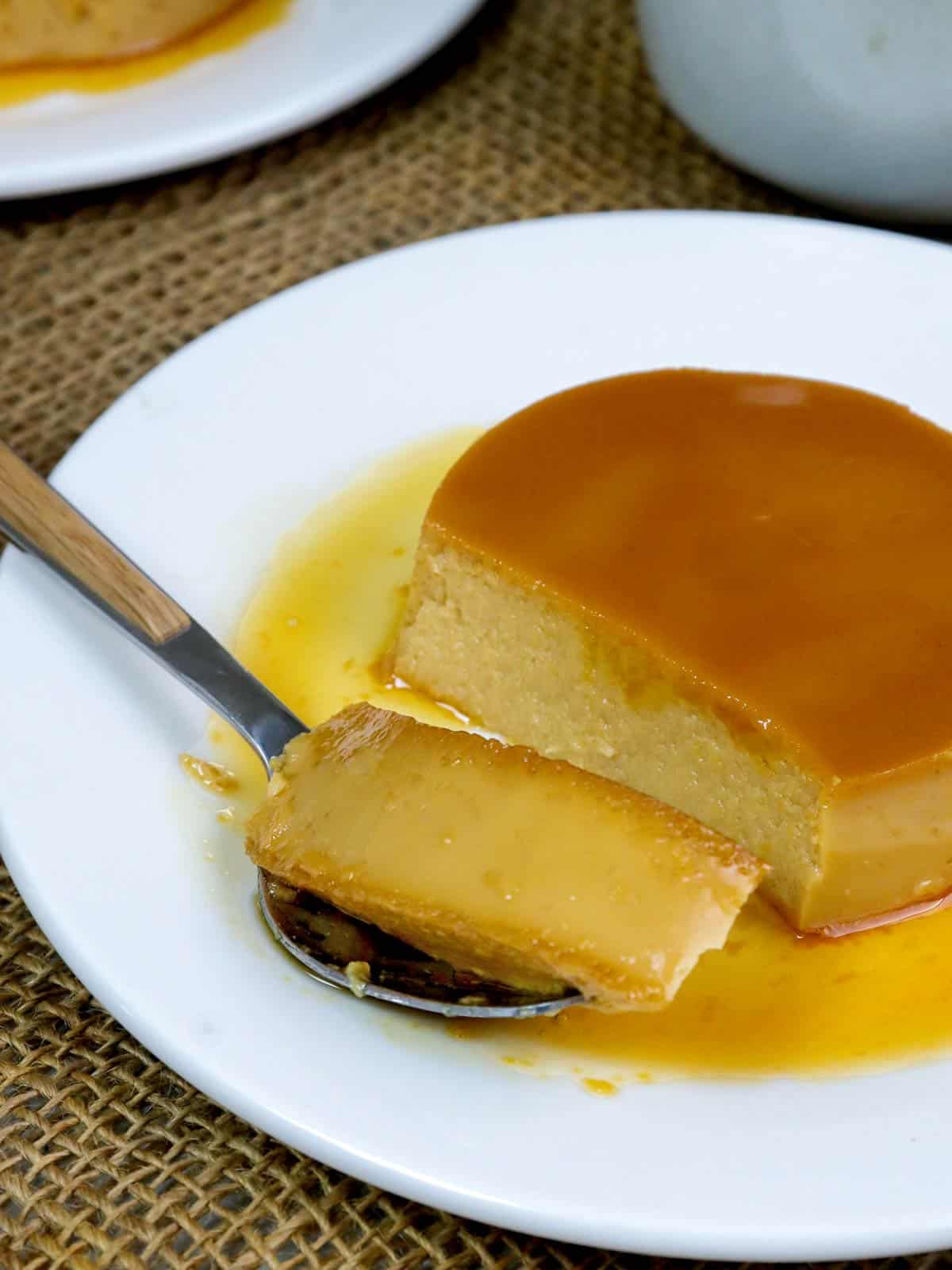 eating Dulce de Leche Flan with a spoon on a white serving plate.