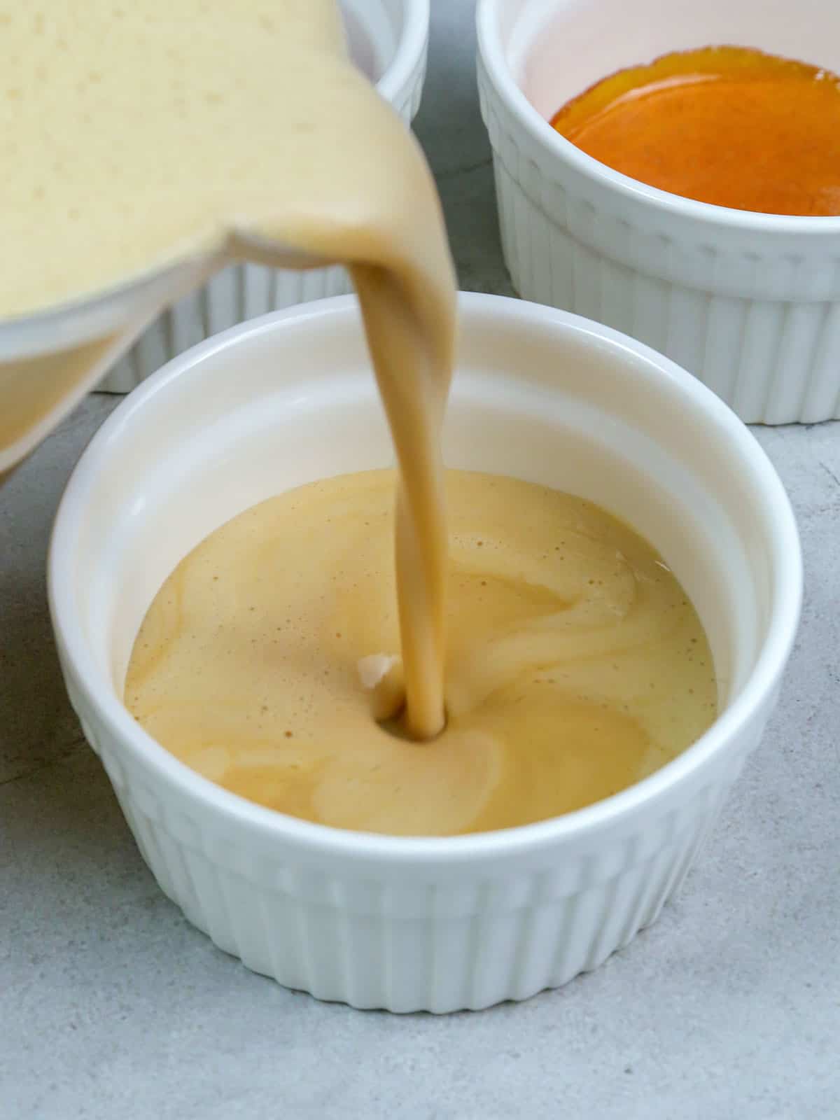 pouring flan mixture in a white ramekin.