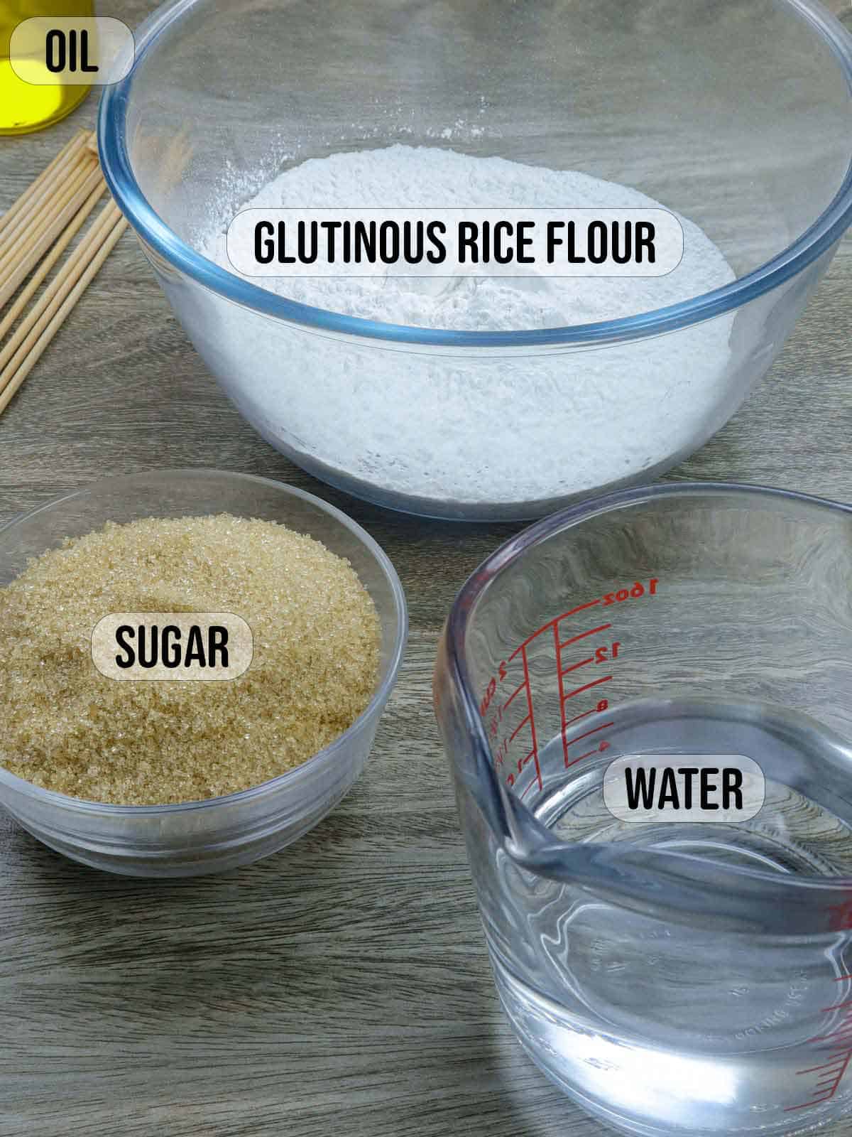 glutinous rice flour in a bowl with oil, bowl of brown sugar and a measuring cup of water in the background.