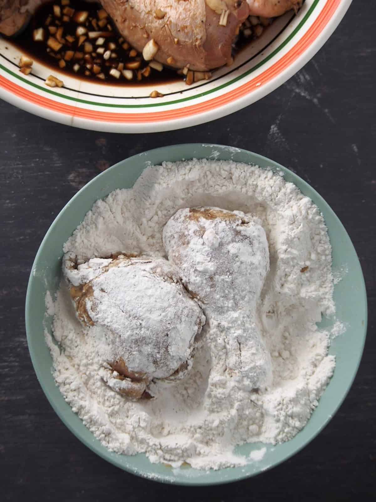 coating marinated chicken pieces with seasoned flour and cornstarch in a blue bowl.