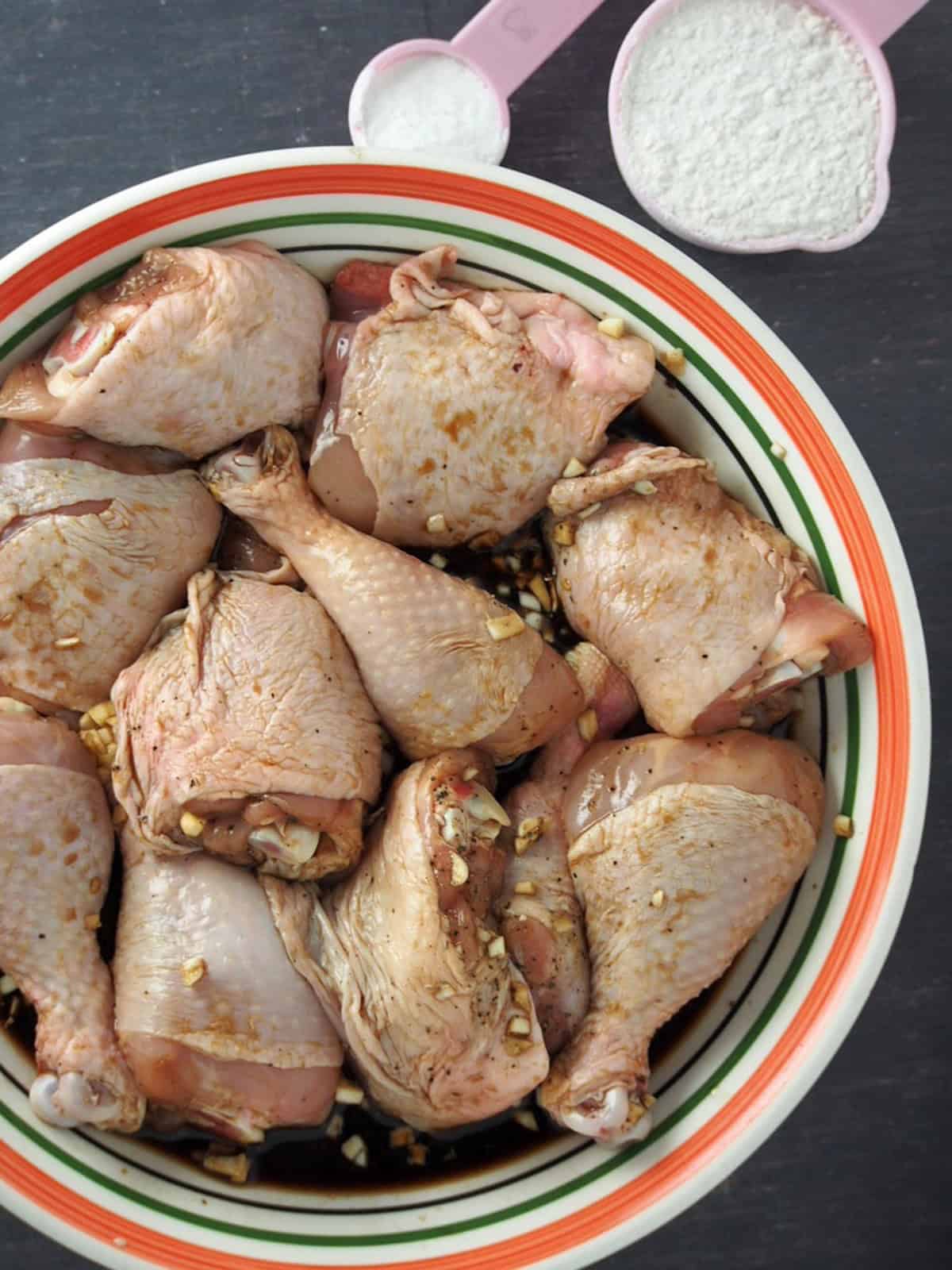 Chicken pieces marinated in citrus, soy sauce, garlic and pepper in a bowl.