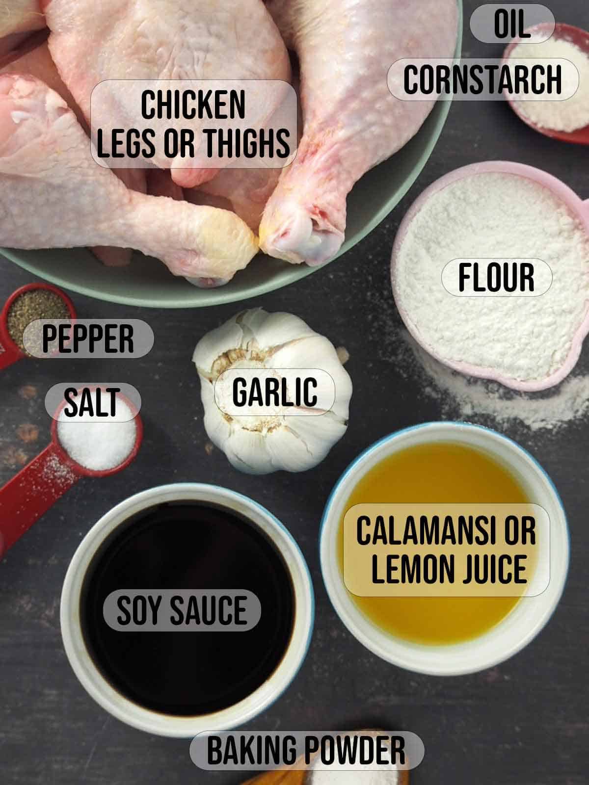 chicken legs and thighs in a large bowl with flour, cornstarch, calamansi juice, garlic, soy sauce, salt, pepper, baking powder in the background.