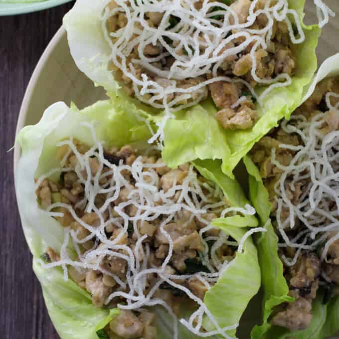 Chicken lettuce cups with crunchy vermicelli noodles on a white plate.