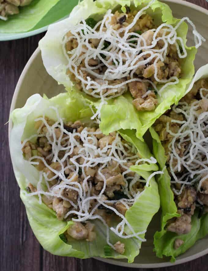 Chicken lettuce cups with crunchy vermicelli noodles on a white plate.