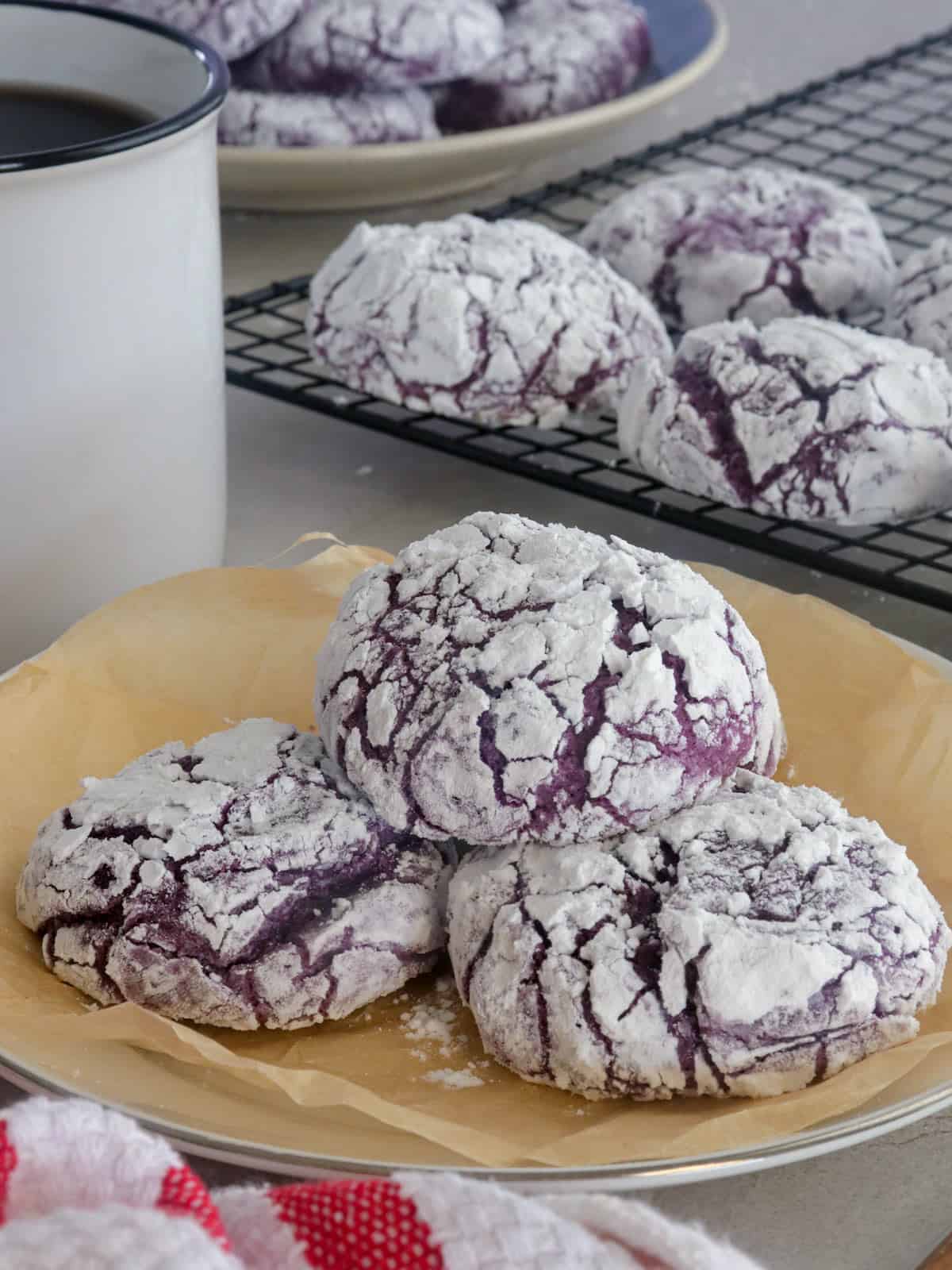 purple yam crinkle cookies on a parchment-lined plate with a cup of coffee in the background.