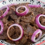 Filipino beefsteak with onions in a white serving bowl.