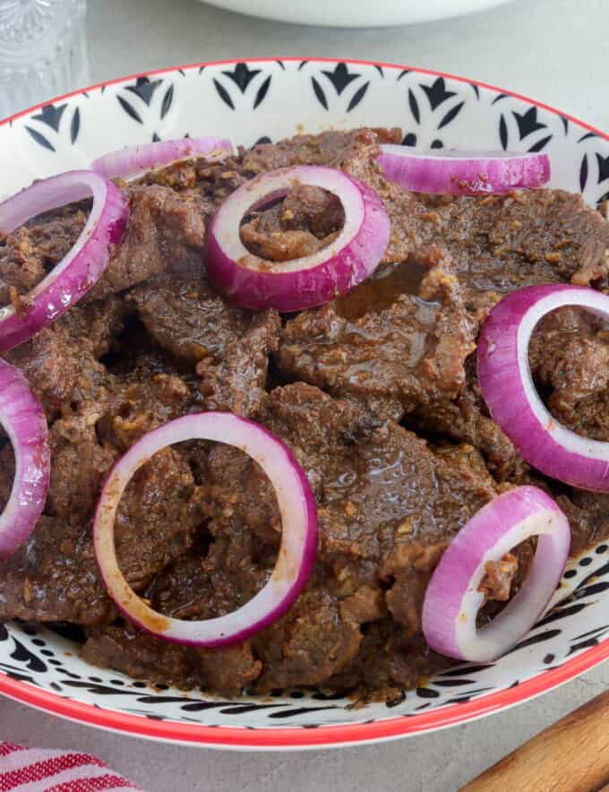 Filipino beefsteak with onions in a white serving bowl.